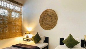 A hotel room with two beds, a woven wall hanging, and a nightstand with a lamp.