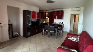 Een ruime woonkamer met een rode bank, een eettafel met stoelen, een keuken met rode kastjes en een betegelde vloer.