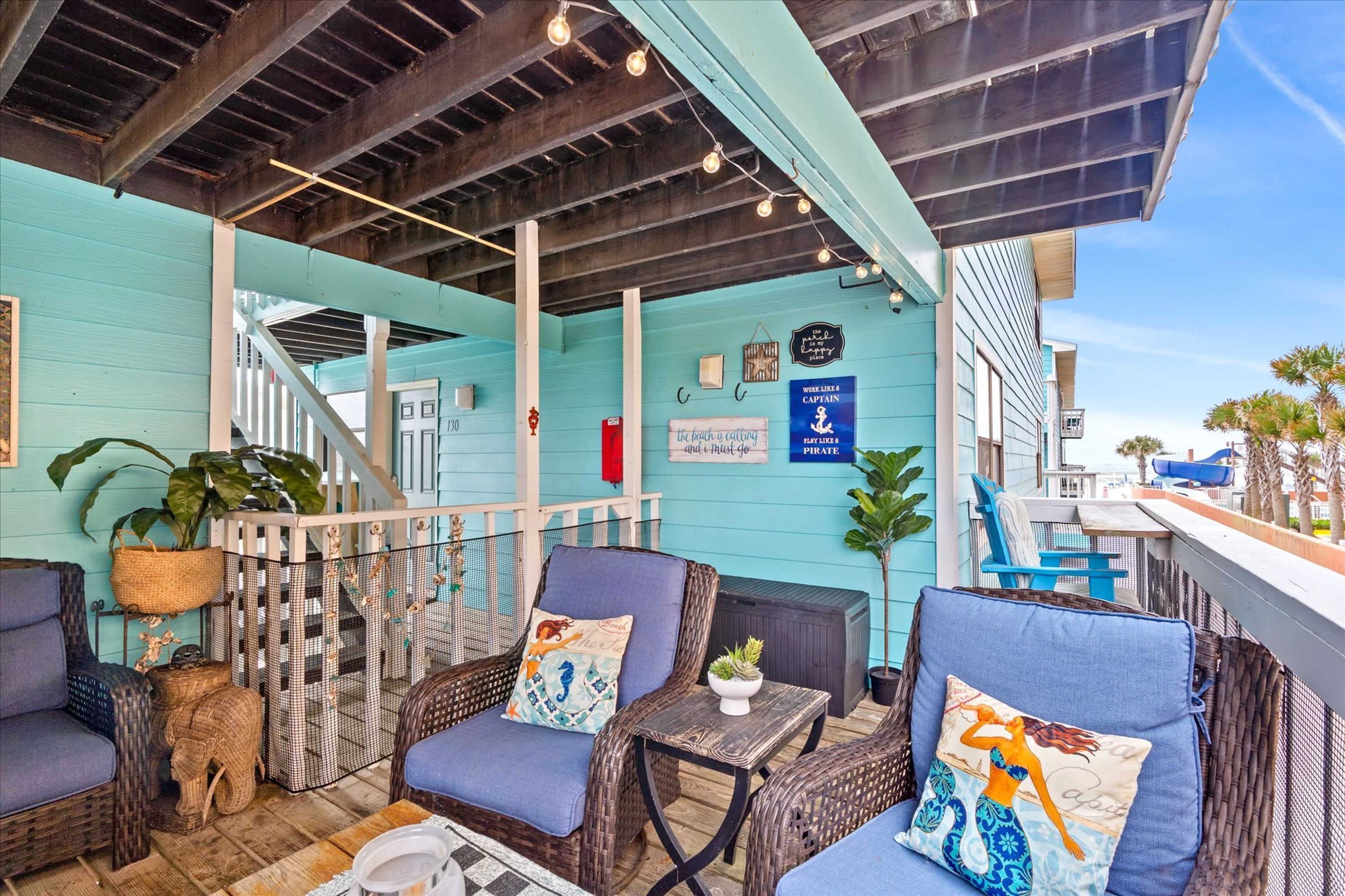 A covered outdoor seating area with wicker furniture, a staircase, and a view of the ocean.