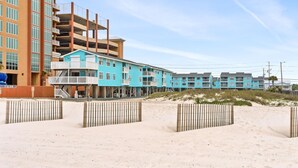 Un hôtel en bord de mer, avec plusieurs étages, une plage de sable en premier plan et un ciel dégagé.