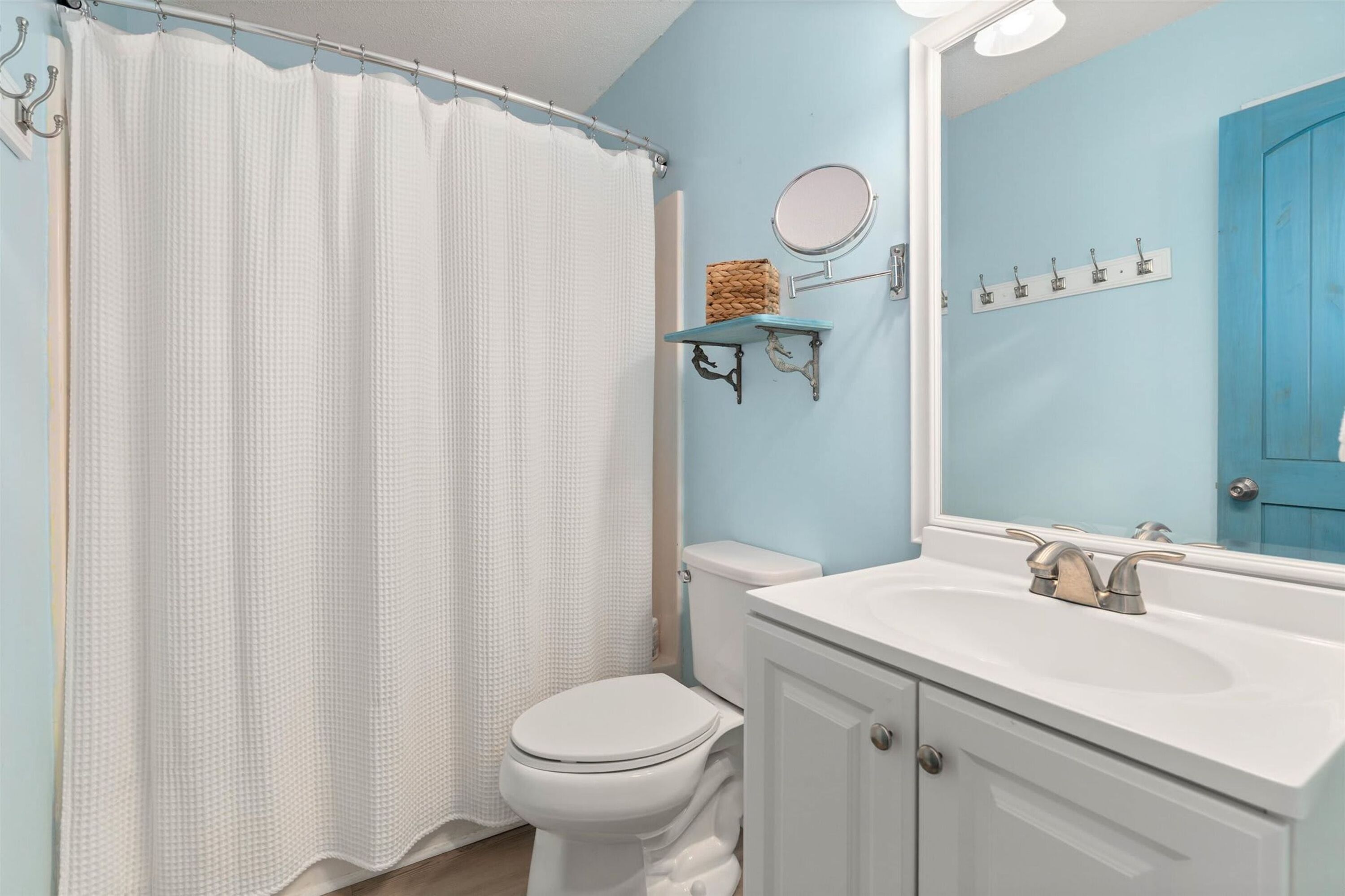 A bathroom with a white toilet, a white sink, a blue wall, a shower curtain, a mirror, and a towel rack.