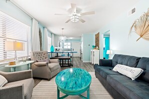 A living room with a sofa, armchair, and round coffee table. - Coastal Condo Steps From the Beach (Gulf Shores)