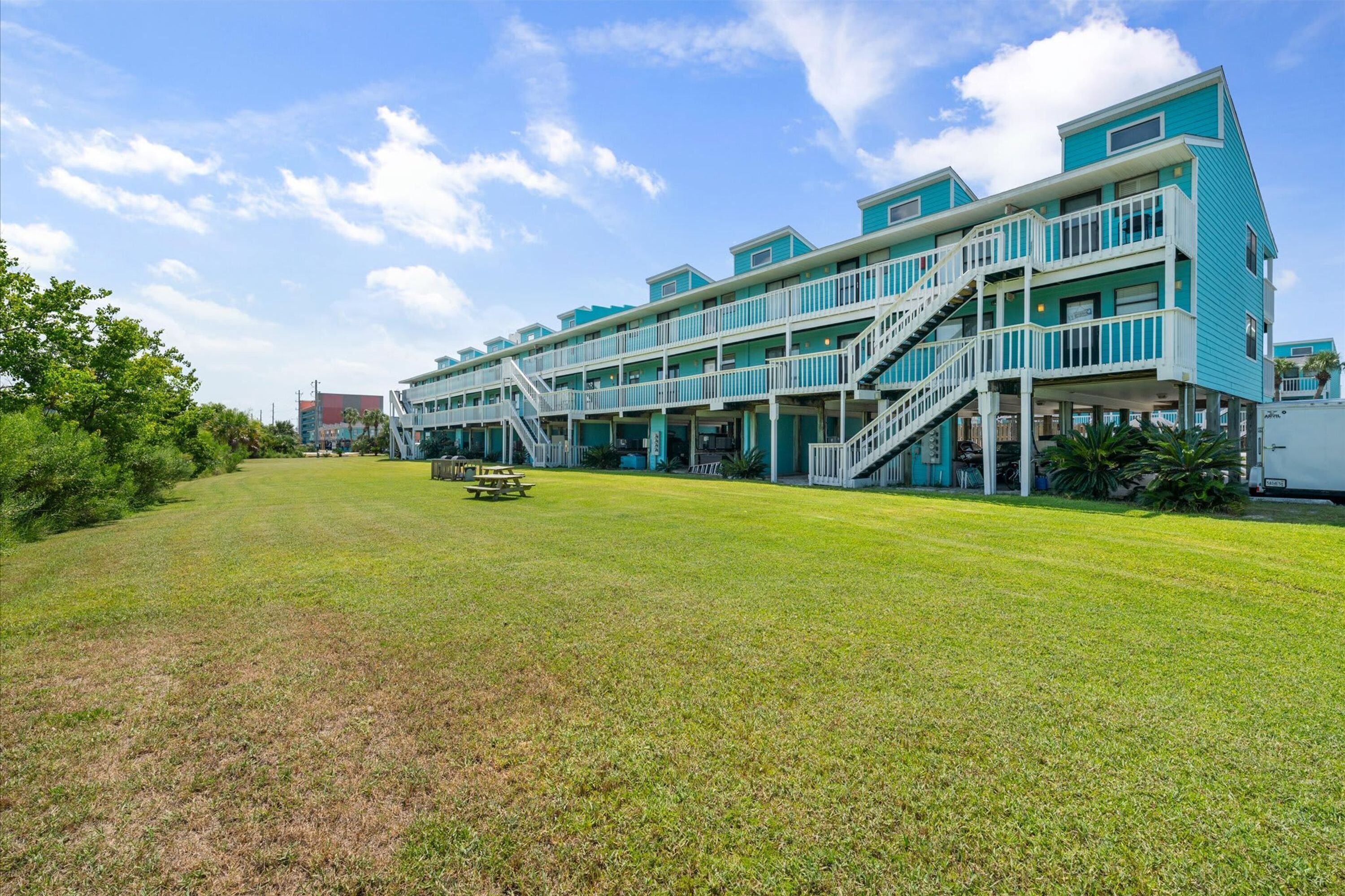 A multi-story building with a flat roof, a grassy lawn, and a picnic table.