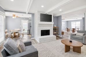 A modern living room with a fireplace, grey sofas, a dining area, and a TV mounted on the wall. - 3BR Family Home Near AFB ASU Riverwalk Downtown (Montgomery)