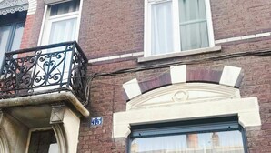 Un bâtiment en briques doté d’une grande fenêtre, d’un balcon orné de balustrades en fer forgé et d’une porte avec une poignée décorative.