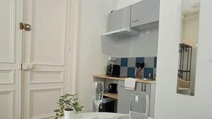 Un coin repas avec une table ronde dressée pour deux personnes, une porte blanche et une cuisine en arrière-plan.