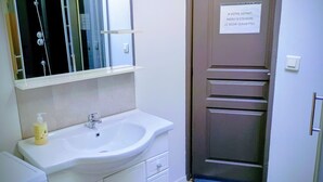 Un baño con lavamanos, espejo y ducha. Hay un cartel en la puerta.