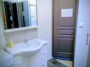 Een badkamer met een wastafel, spiegel en douche. Er hangt een bordje op de deur.