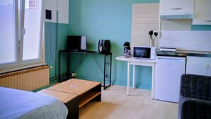 Una habitación compacta con cama, una mesita, kitchenette y ventana.