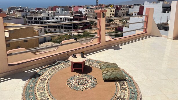 Een balkon met een kamerkleed, een tafeltje en een kussen.