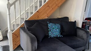 Een zwarte modulaire bank met een gekussend kussen, een houten trap met witte spijlen, en een stenen vloer.