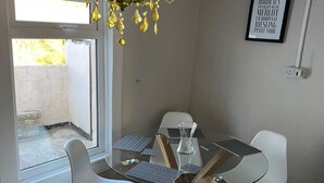 Een eetruimte met een glazen tafel, witte stoelen, een kroonluchter en een lijst met wijnen in een lijst aan de muur.