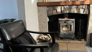 Een stenen openhaard met een houtkachel, een zwarte leren fauteuil en een welkomstbord erboven.