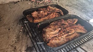 Een barbecue met vlees dat gaart, een bakstenen muur en een kleine hoeveelheid kolen.