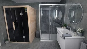 Een moderne badkamer met een glazen douchecabine, een inloopkast met houten deuren en een wit wastafelmeubel met spiegel.