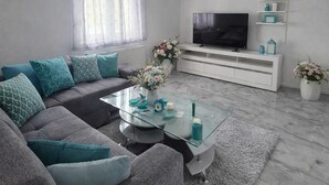 Een moderne woonkamer met een hoekbank, een glazen salontafel, een flatscreen televisie en decoratieve objecten.
