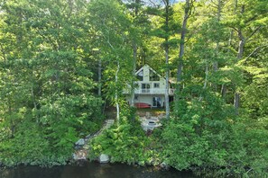 Ein Haus, umgeben von dichtem Wald, mit sichtbarer Terrasse und Feuerstelle.