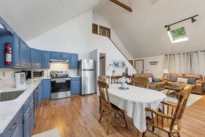 Eine moderne Küche mit blauen Schränken, ein Essbereich mit Tisch und Stühlen, ein Wohnzimmer mit einer Couch und eine Treppe.