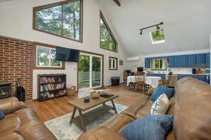 Ein geräumiges Wohnzimmer mit Kamin, Bücherregal, Essbereich und Küche mit blauen Schränken.