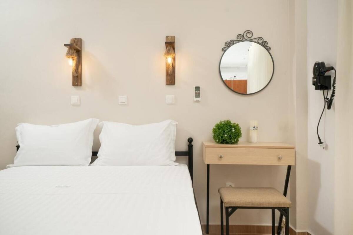 Un dormitorio con cama, mesita de noche, silla, espejo montado en la pared y dos apliques.