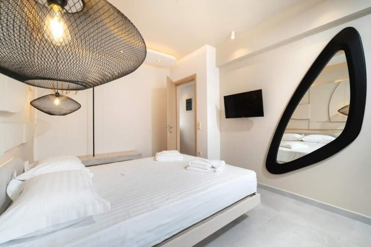 Un dormitorio moderno con cama, un espejo grande, un televisor de pantalla plana y una lámpara de techo original.
