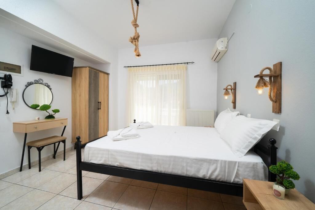 A bedroom with a bed, bedside table, desk, chair, TV, and a window with curtains.