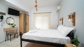 A bedroom with a bed, bedside table, desk, chair, TV, and a window with curtains.