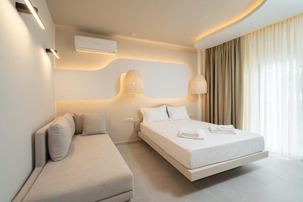 A modern hotel room with a bed, a sofa, and a wall-mounted air conditioner.