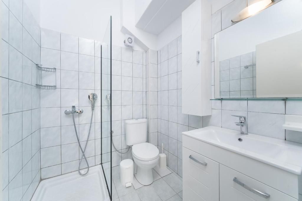Un baño moderno con azulejos blancos, cabina de ducha de vidrio, inodoro y lavabo con espejo.