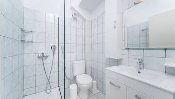 Un baño moderno con azulejos blancos, cabina de ducha de vidrio, inodoro y lavabo con espejo.
