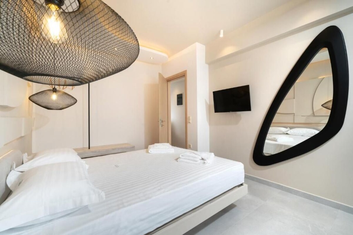 A modern bedroom with a bed, a large mirror, a flat-screen TV, and a unique ceiling light fixture.