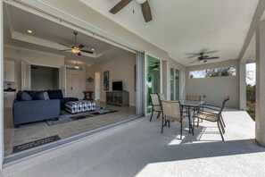 Ein großzügiger Wohnbereich mit Sofa, Hocker und einem Esstisch mit Stühlen. Deckenventilatoren und ein Fernseher sind vorhanden.