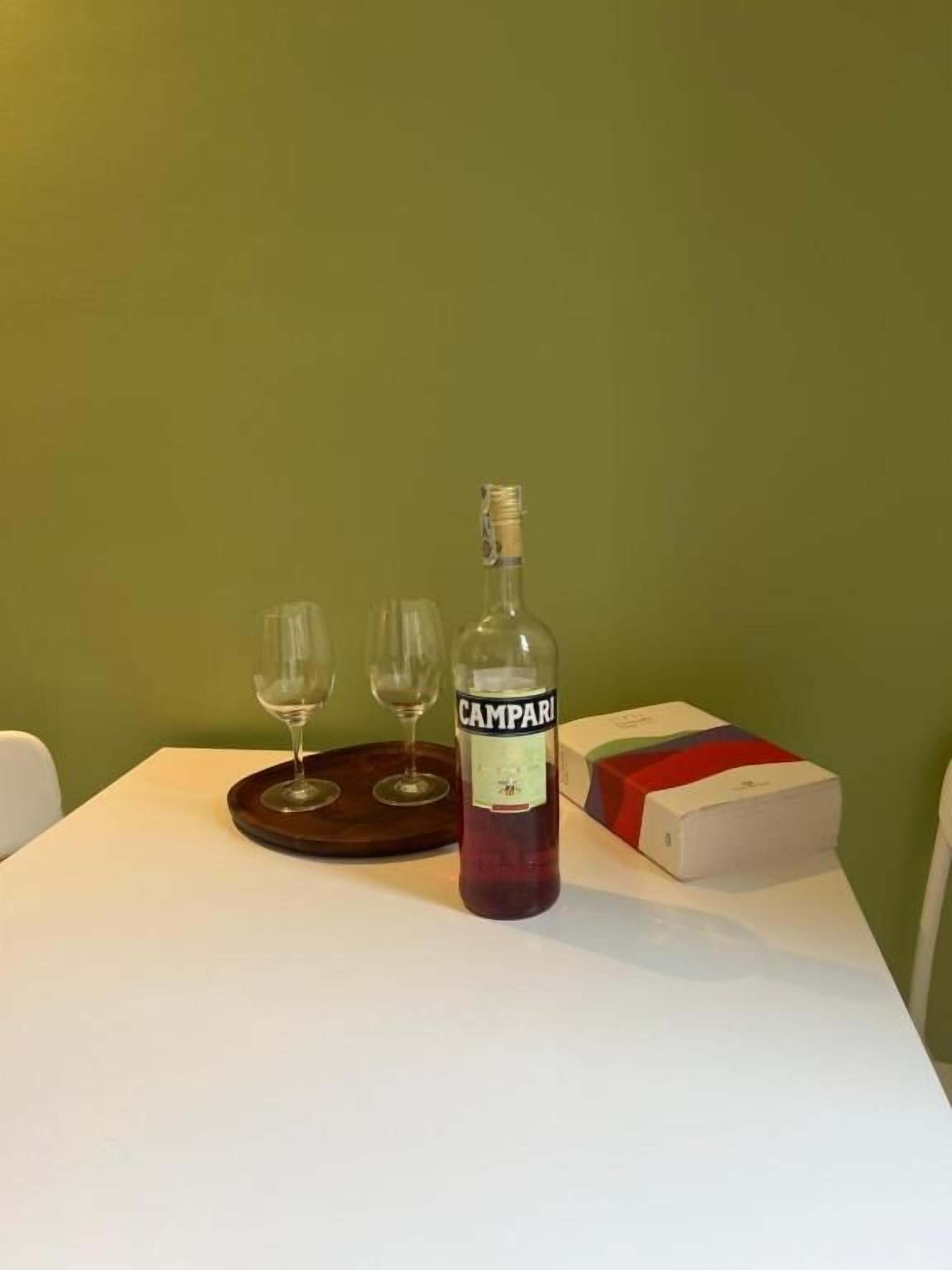 Un tavolo con una bottiglia di Campari, due bicchieri da vino e una scatola.