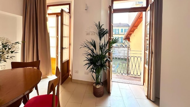 A room with a wooden dining table, a red chair, a potted plant, and a balcony with a metal railing. - Luma Novara (Novara)