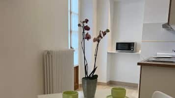 A modern kitchen with white appliances, a dining table with green cups, and a potted orchid.