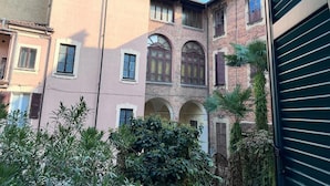 A courtyard with buildings, arched windows, and a palm tree. - Luma Novara (Novara)