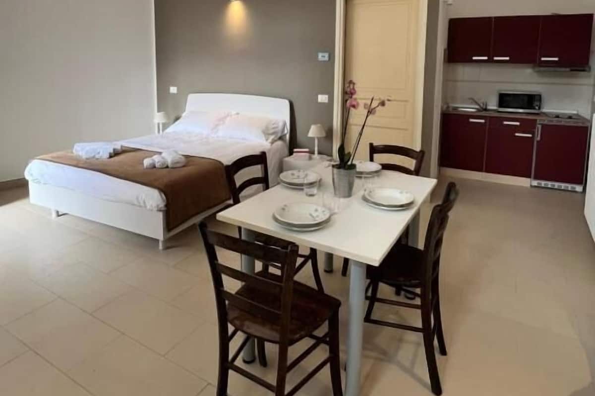 Ein Hotelzimmer mit Bett, Esstisch mit Stühlen, einer kleinen Küchenzeile und einer Tür.