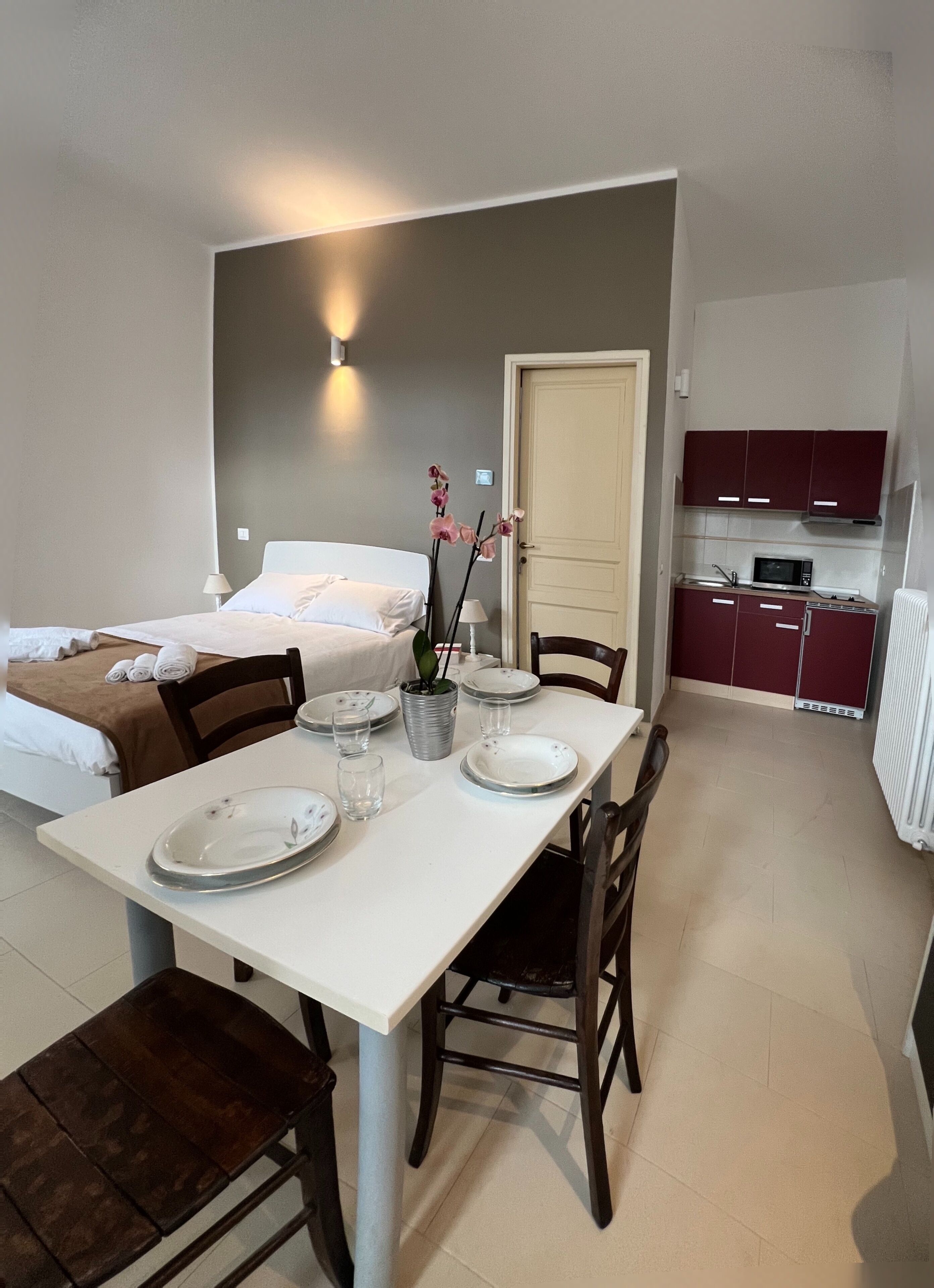 A compact room with a bed, a dining table with chairs, a small kitchen area, and a door.