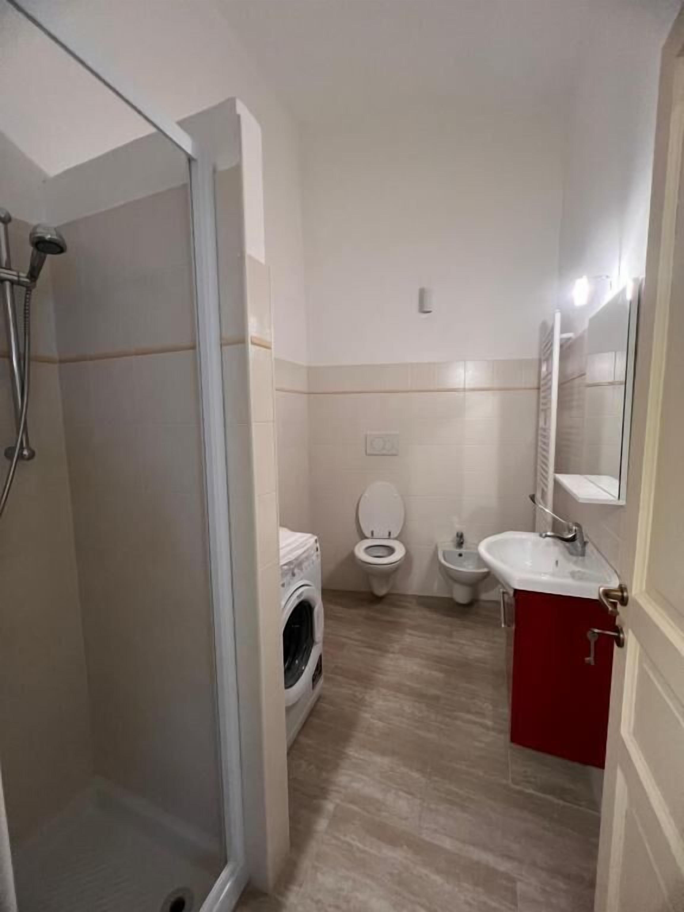 A bathroom with a shower, toilet, bidet, and a washing machine.