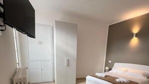 A hotel room with a bed, a TV mounted on the wall, a minibar, and a window. - Luma Novara (Novara)