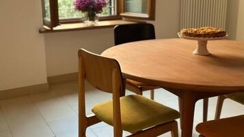 A dining table with a pie on a stand, a chair with a cushion, and a window with flowers.