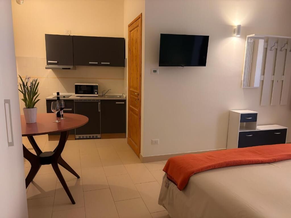 Habitación de hotel compacta con cama, una pequeña mesa de comedor, microondas, televisión y kitchenette.