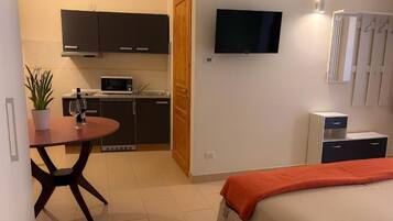 Habitación de hotel compacta con cama, una pequeña mesa de comedor, microondas, televisión y kitchenette.