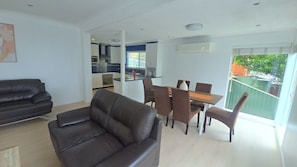 A modern living room with a leather sofa, dining table with chairs, and a kitchen in the background. - Home with water view in Central Coast (Budgewoi)