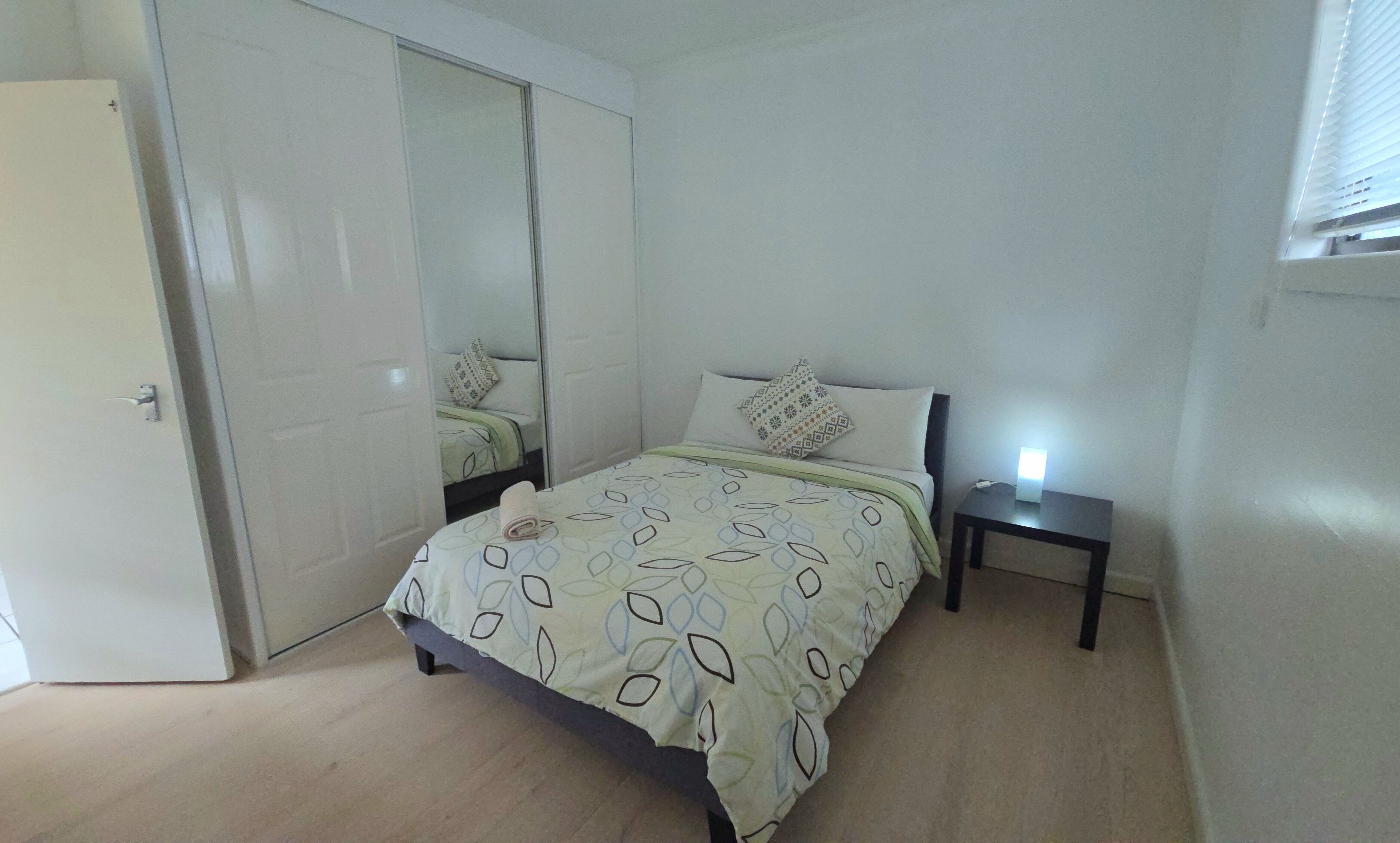 A bedroom with a bed, a bedside table, a mirror, and a door.