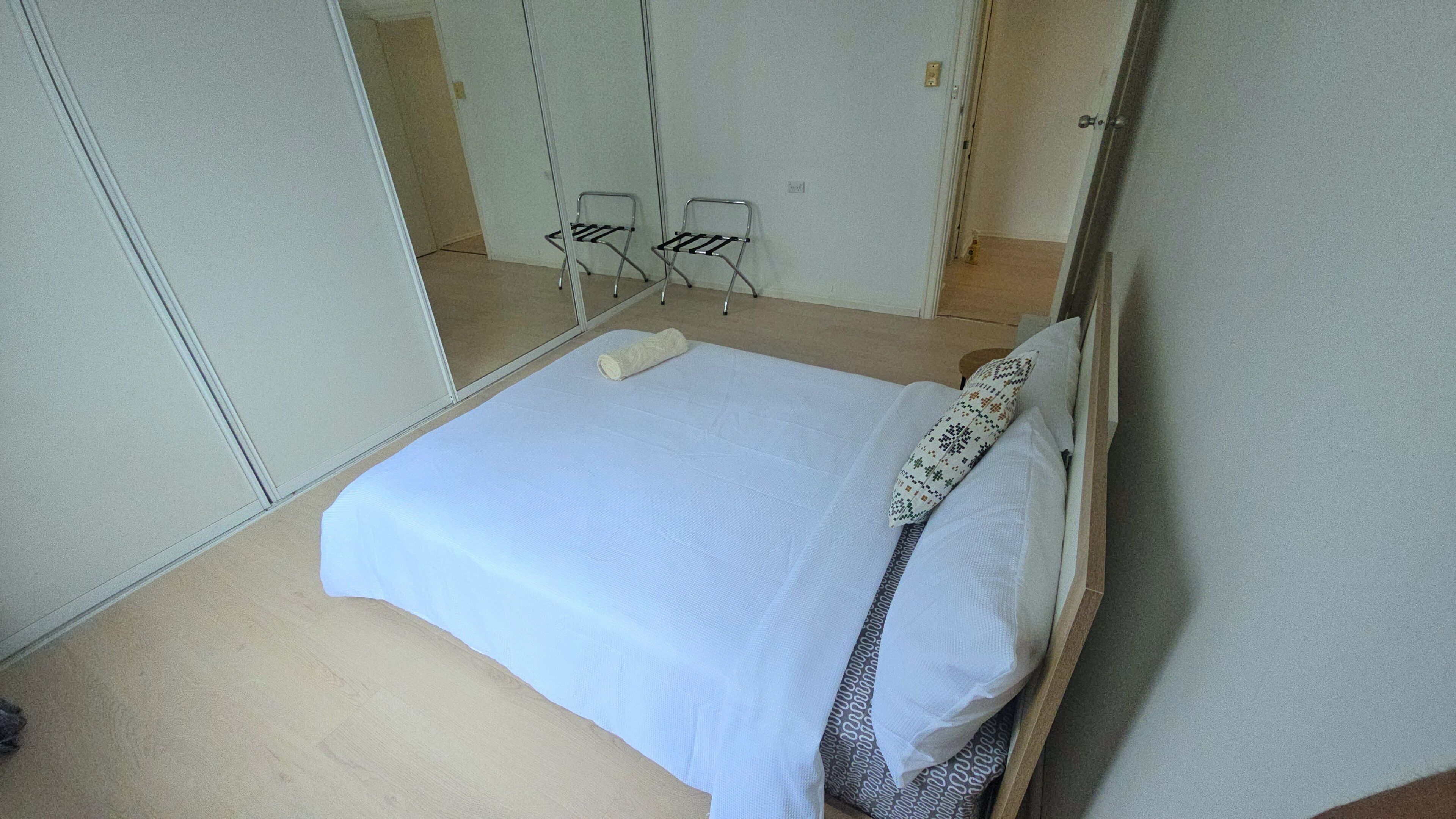 A bedroom with a bed, a pillow, a rolled-up towel, and a mirror.