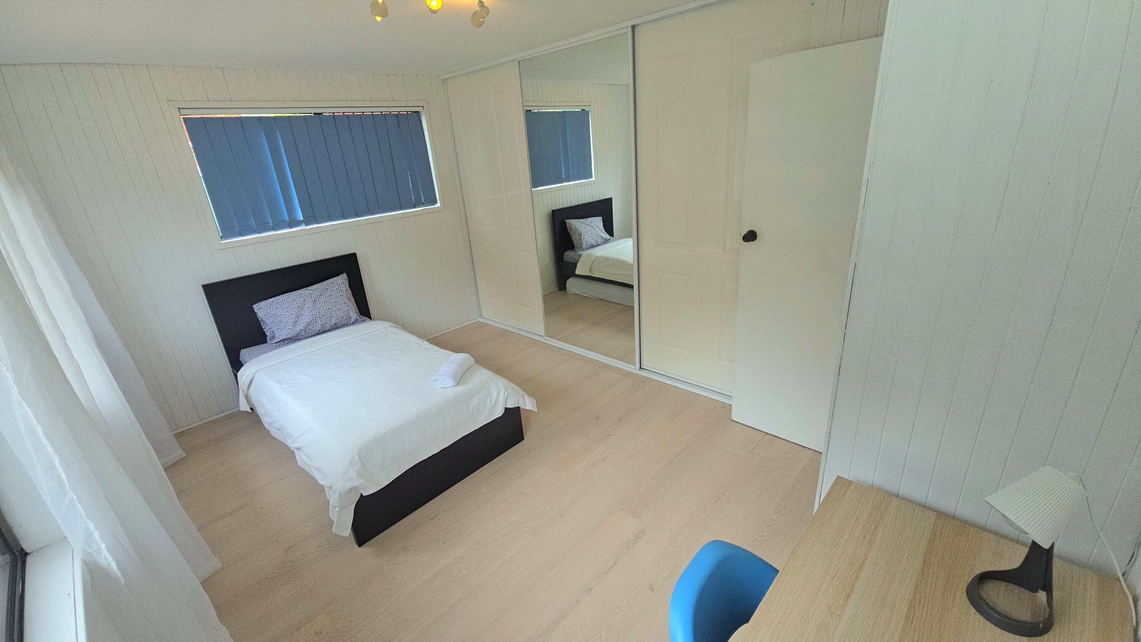 A bedroom with a bed, a chair, a wardrobe, and a window.