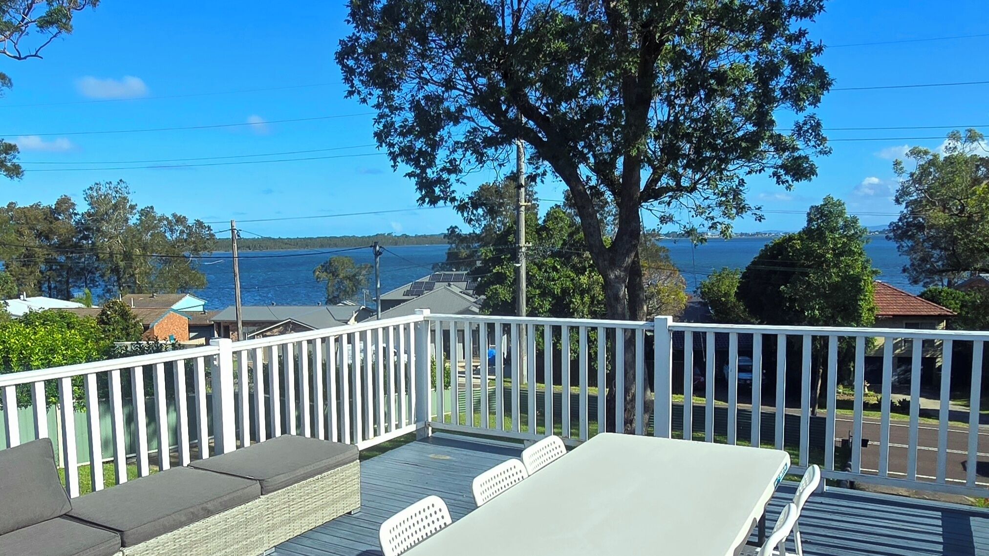 A deck with a table and chairs, overlooking a body of water and houses.