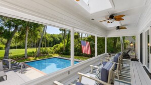 A covered pool area with a view of a lawn and an American flag. - 7 Rum Row - Private Pool, Golf Views & Walk to the Beach in Palmetto Dunes (Hilton Head Island)