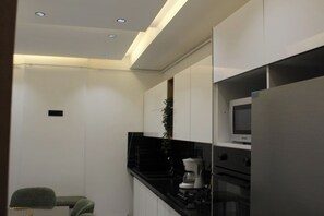 Una cocina moderna con armarios blancos, encimera negra, microondas y cafetera.